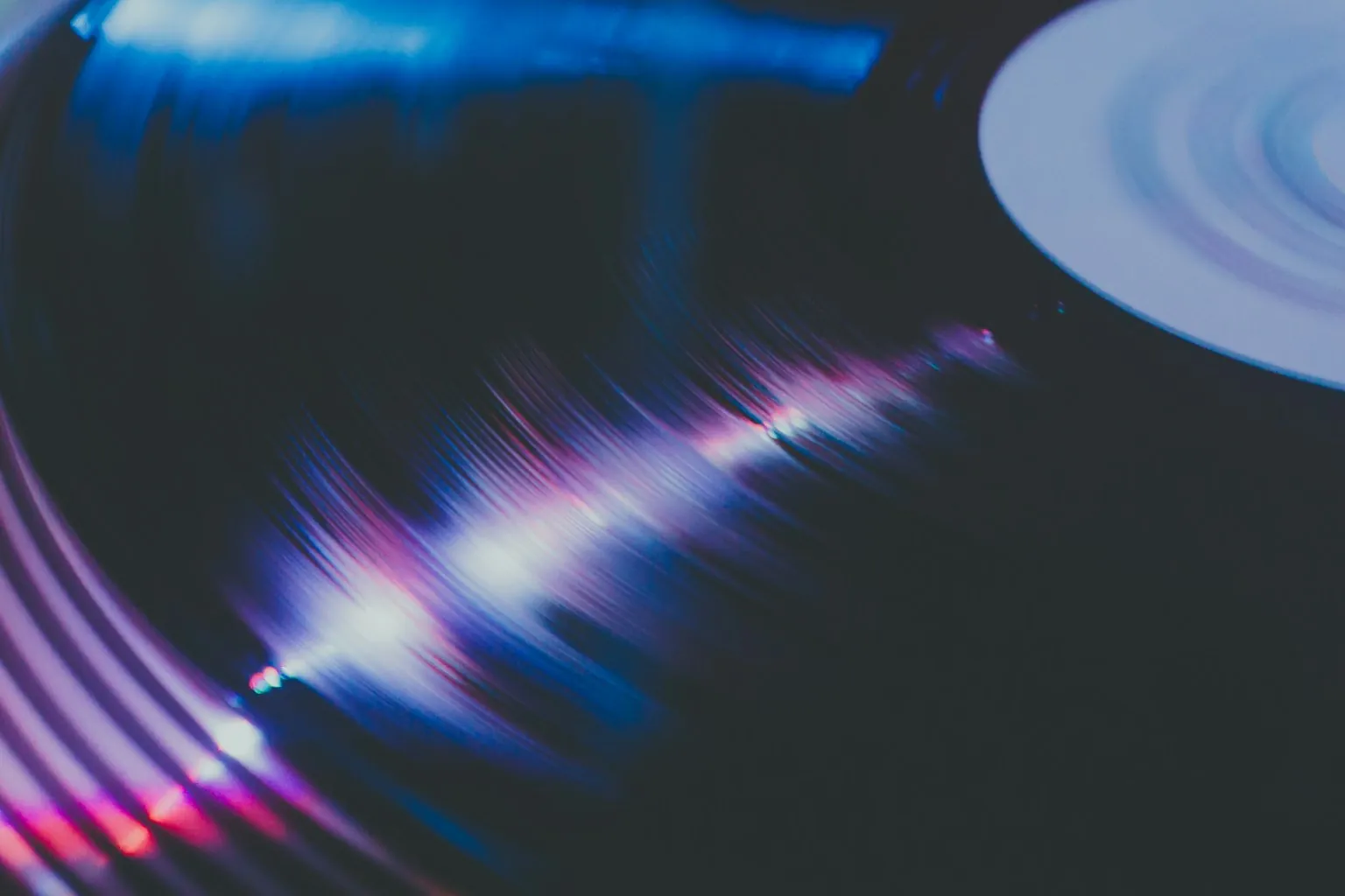 Close-up of a vinyl record spinning on a turntable with purple and blue light reflections on the grooves, evoking the nostalgia of Classic Hits radio