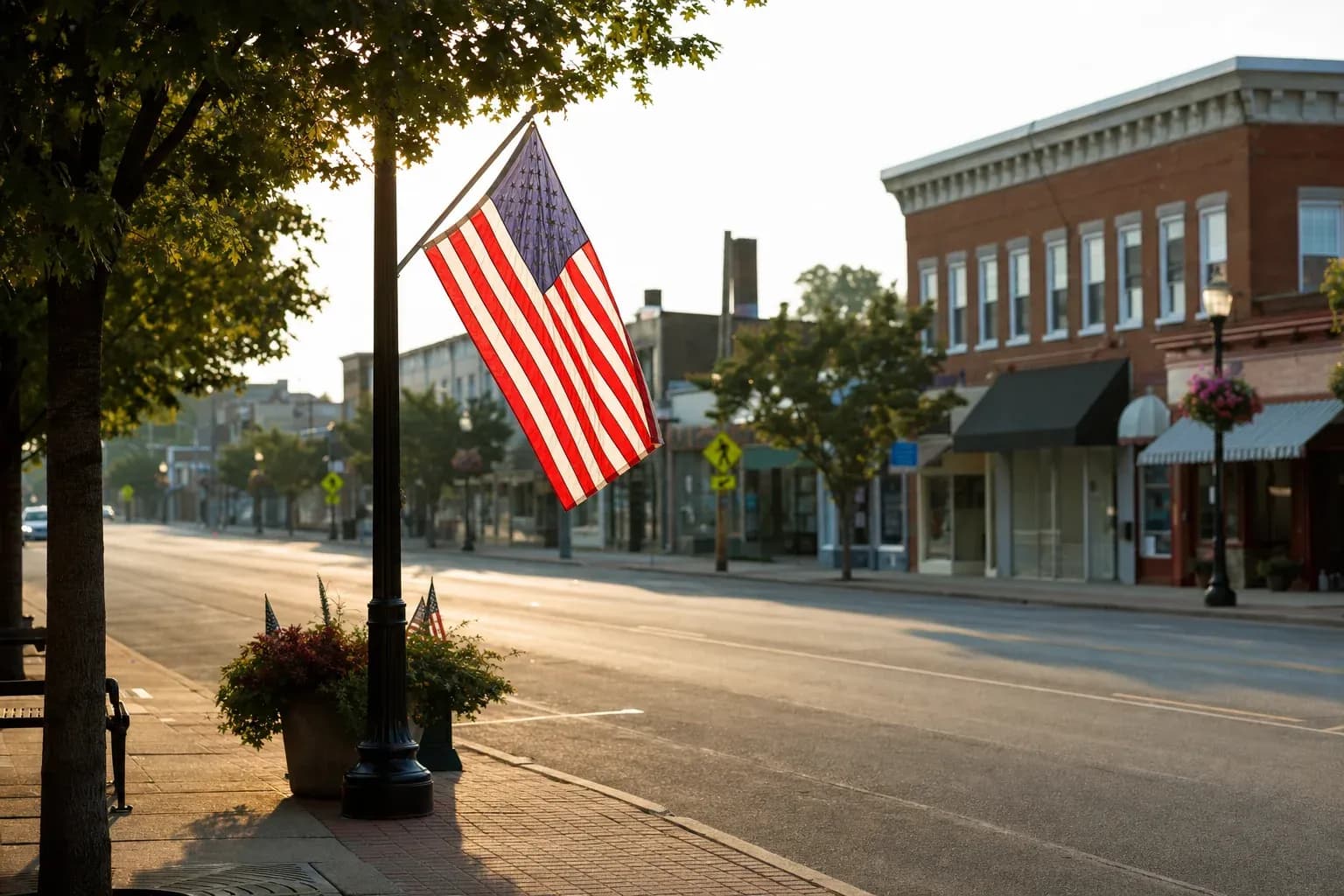 A single American flag on a small-town main street pole in early summer morning light, a quiet understated Flag Day moment for radio programming