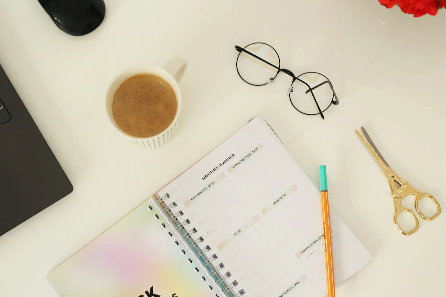 Overhead flat-lay of a content planning workspace with an open notebook, a cup of coffee, pen, scissors, and eyeglasses arranged on a sunlit surface
