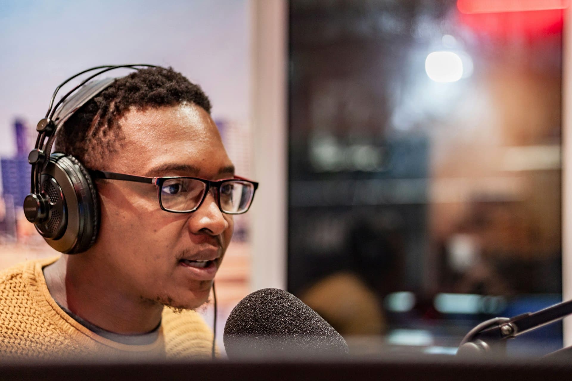 A radio personality in headphones at a studio microphone, leaning in to perform
